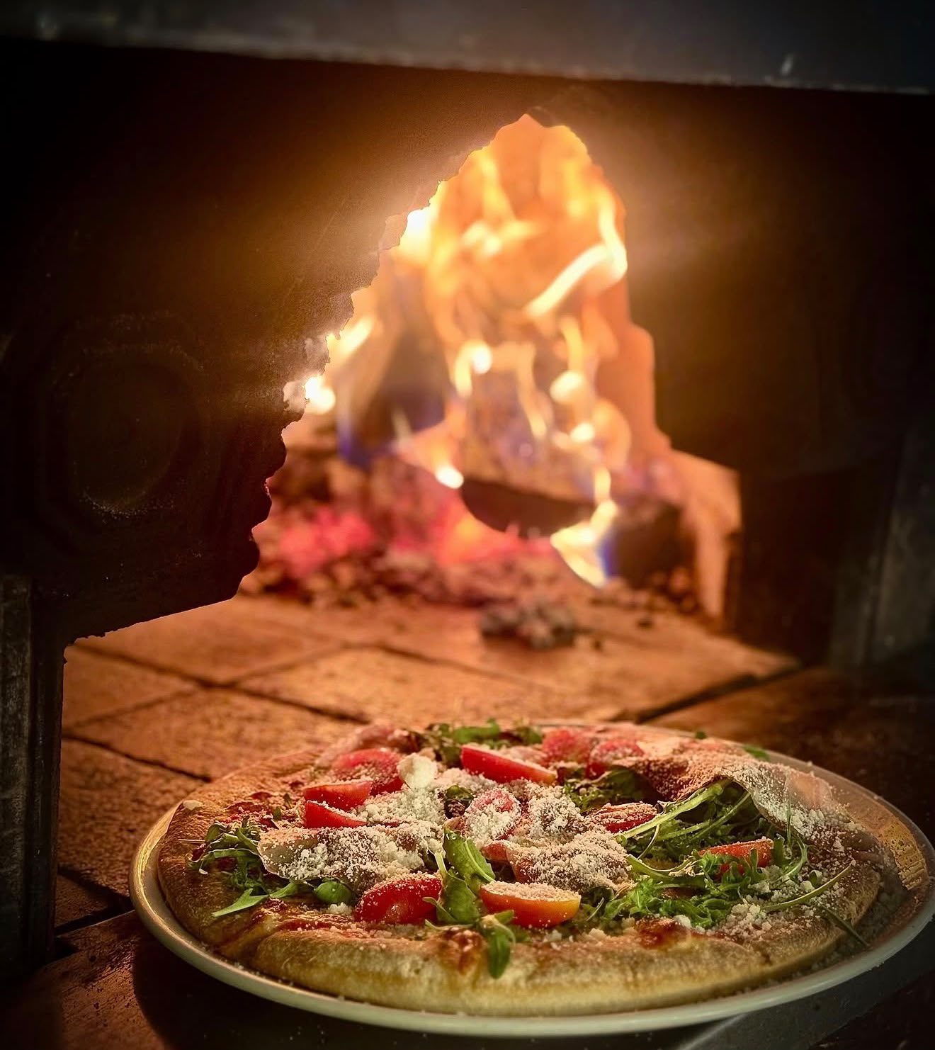 Pizza z rukolą i pomidorkami przed piecem opalanym drewnem