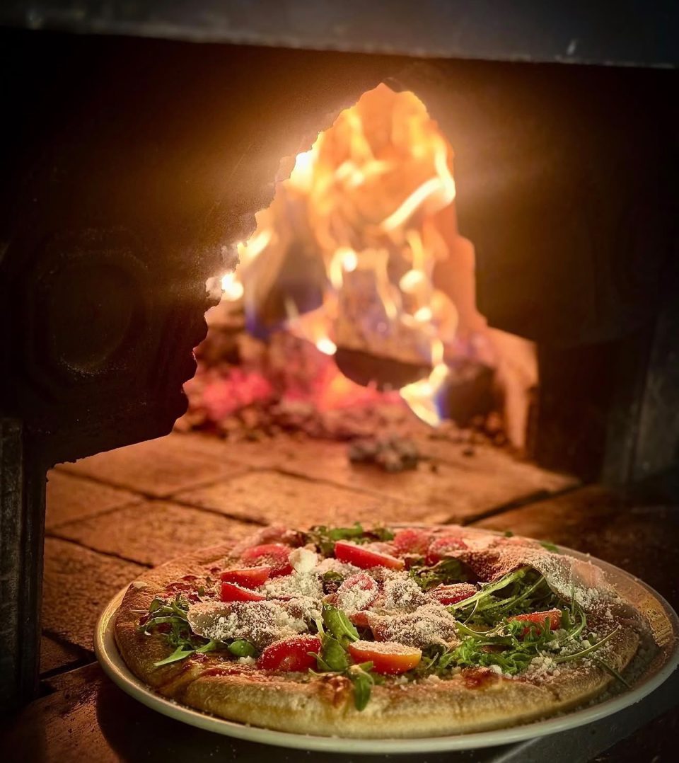 Pizza z rukolą i pomidorkami przed piecem opalanym drewnem